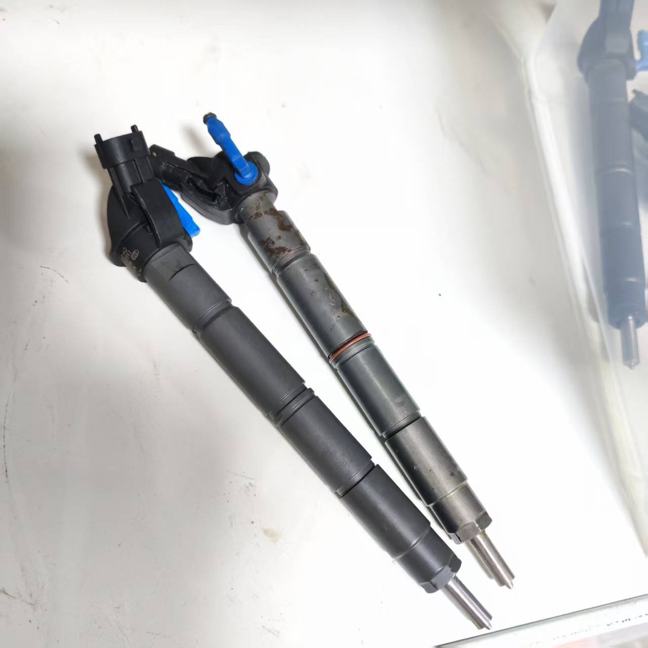 Refurbished diesel injectors showing a black-finished piezo injector beside a visibly corroded used core